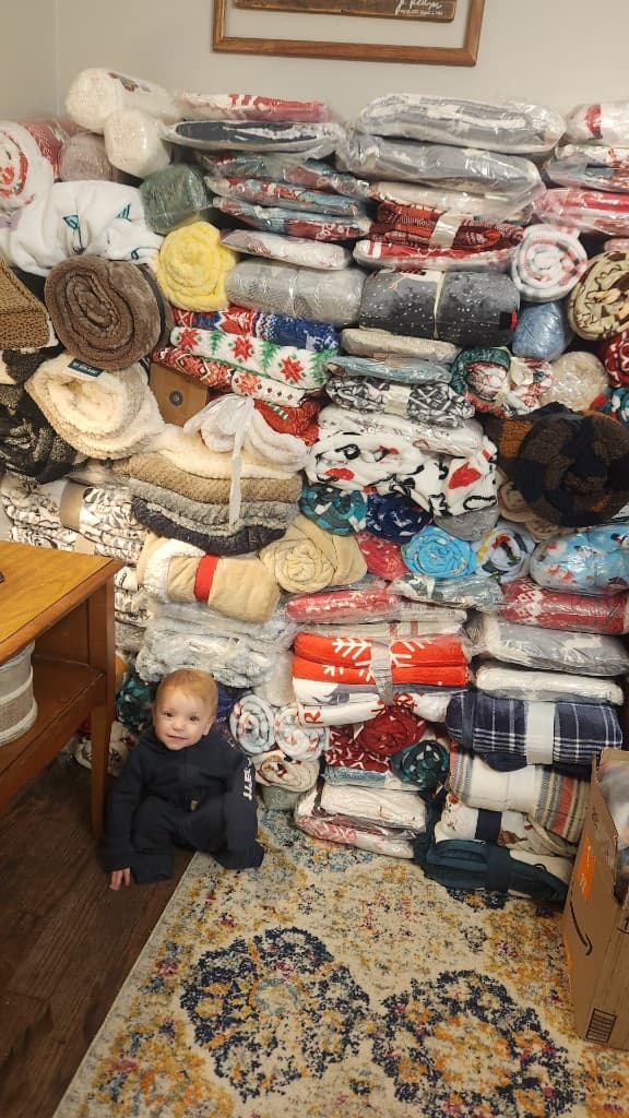 A child sitting in front of stacks of blankets.
